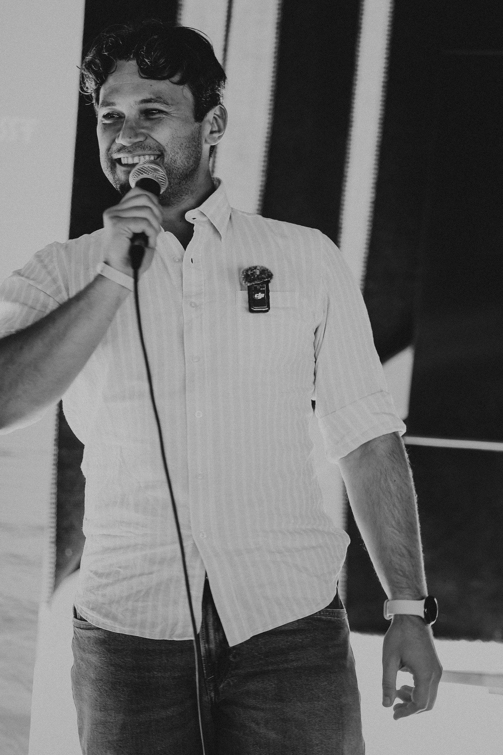 Black-and-white portrait of Daniel Duma smiling with a microphone on stage